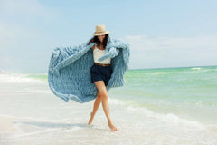 Model wearing the Hugs Alaskan Blue Blanket on the beach, showcasing its cozy and stylish design.