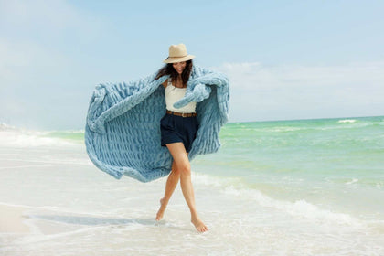 Model wearing the Hugs Alaskan Blue Blanket on the beach, showcasing its cozy and stylish design.