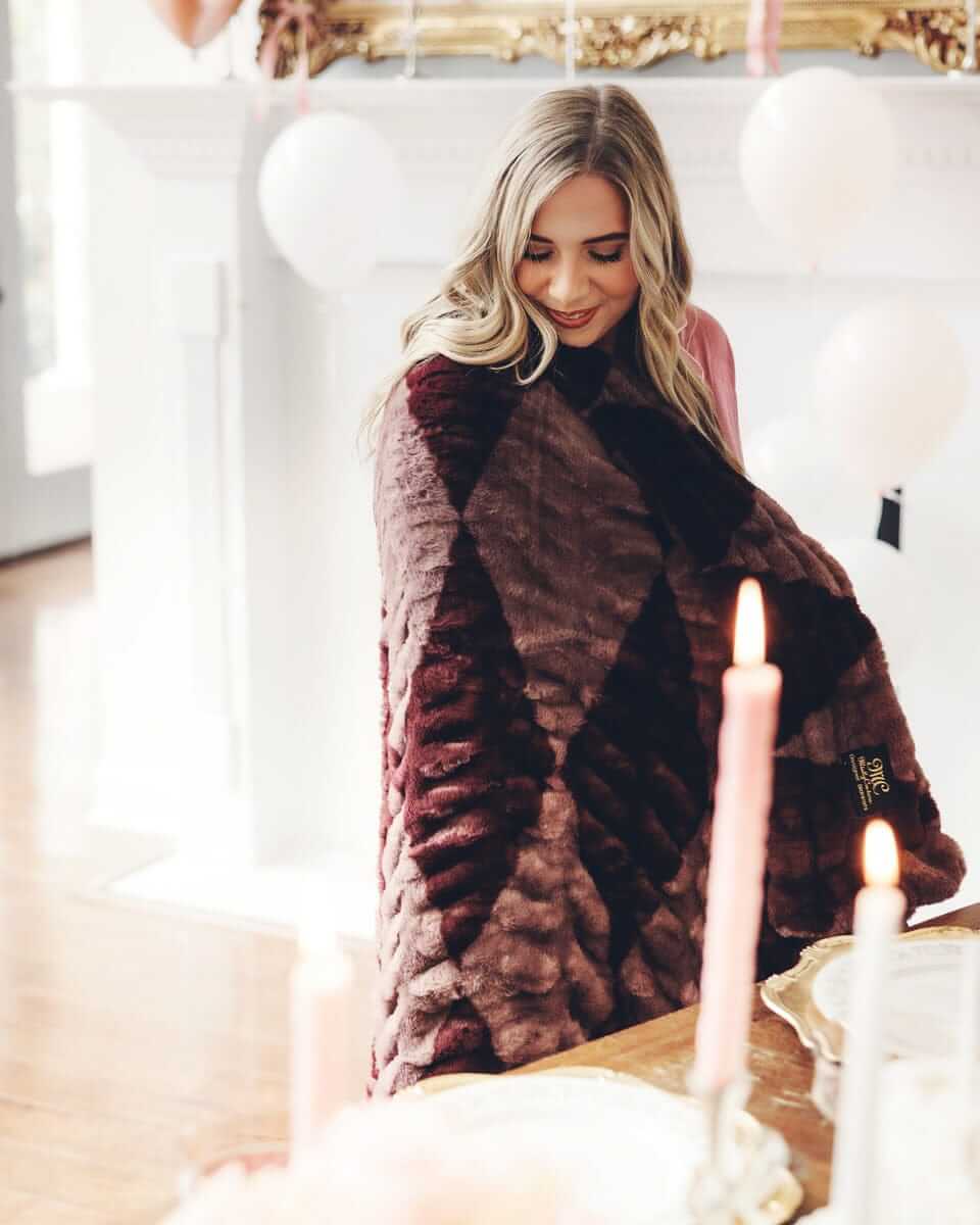 Woman wrapped in a plush Minky Couture blanket, looking down and smiling.