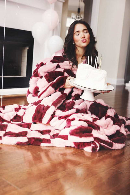 Woman holding a cake while wrapped in a Hugs Devin Pink Checkered blanket.