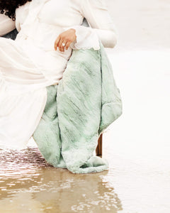 Person wrapped in a light green blanket sitting on a wooden bench.