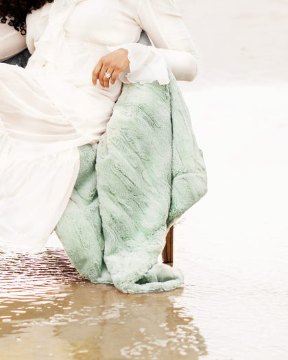 Person wrapped in a light green blanket sitting on a wooden bench.