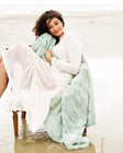 Woman sitting on a chair with a light green blanket draped over her, surrounded by water.