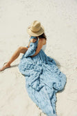 Woman relaxing on the beach wrapped in the Hugs Alaskan Blue Blanket, enjoying sunny vibes.