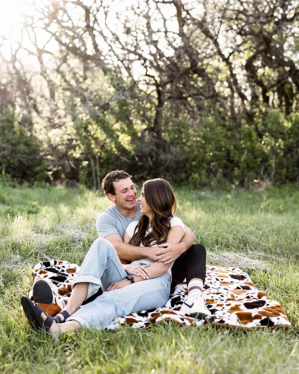 Couple enjoying a moment on the Everywhere Blanket Brown Cow in a scenic grassy area.