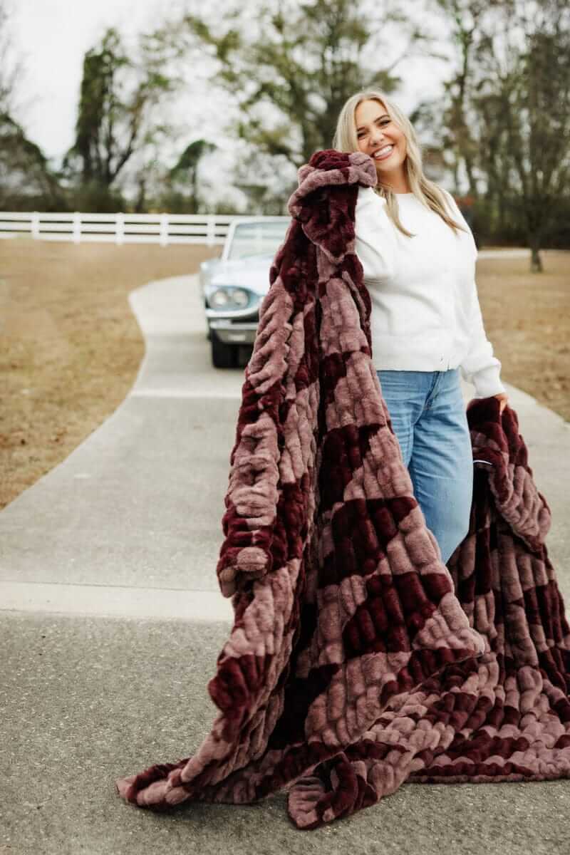 Woman holding a plush Hugs Shelby Mulberry Diamond blanket, smiling.
