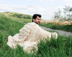 Man sitting outdoors wrapped in a Minky Couture Ultra Sorbet Sand Blanket against a grassy landscape.