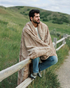 Man sitting on a fence outdoors, wrapped in a Sorbet Milk Chocolate Blanket, enjoying the cozy comfort.