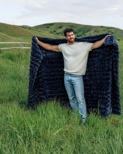 Man showcasing the Ultra Sorbet Navy weighted blanket in a grassy outdoor setting, highlighting its plush texture and deep blue color.