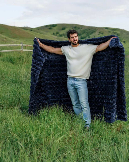 Man showcasing the Ultra Sorbet Navy weighted blanket in a grassy outdoor setting, highlighting its plush texture and deep blue color.