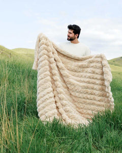 Man holding the Ultra Sorbet Sand weighted blanket outdoors with a soft texture and warm neutral color.