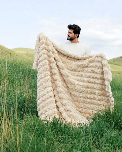 Man holding the Ultra Sorbet Sand weighted blanket outdoors with a soft texture and warm neutral color.