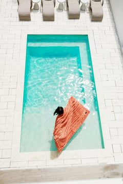 Person relaxing by a pool wrapped in the Ultra Sorbet Tawny Spice Blanket, showcasing its rich coral hue and cozy texture.