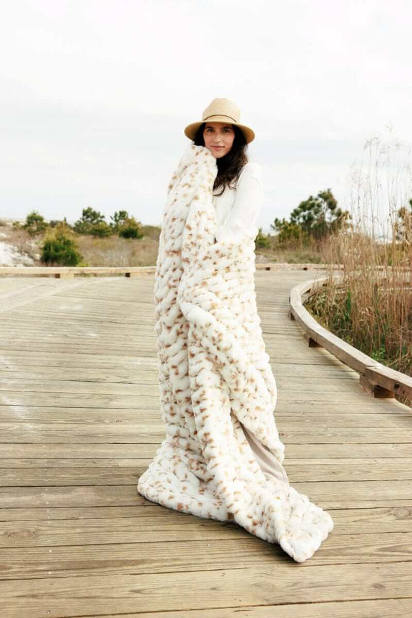 Woman wearing the Hugs Spotted Fawn Blanket on a wooden path, showcasing its cozy softness and stylish design.