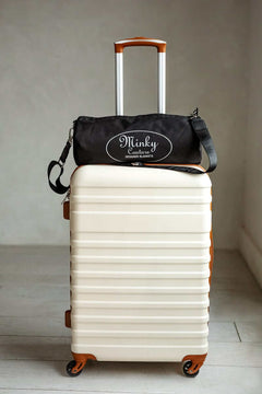 Minky Couture brand blanket duffle bag sitting on top of a cream colored suitcase.
