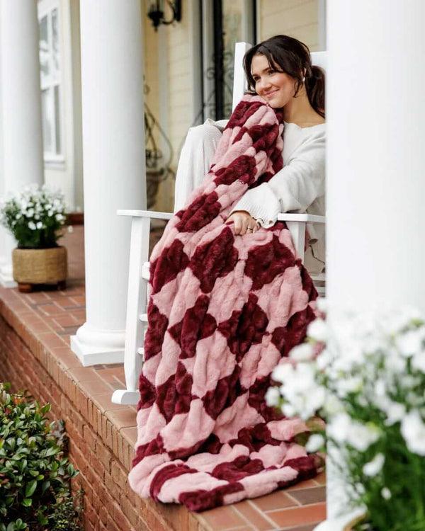 Woman relaxing on a chair, wrapped in a plush Minky Couture Hugs Devin Pink Checkered.