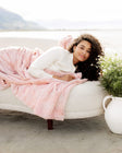 Woman wrapped in a pink blanket on a white couch by a body of water