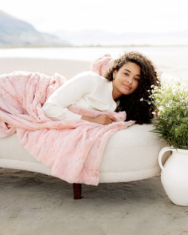 Woman wrapped in a pink blanket on a white couch by a body of water