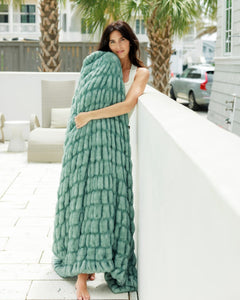 Woman wrapped in a green blanket on a patio with palm trees in the background.