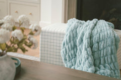 Hugs Willow Blue textured blanket draped over a chair with a neutral background.