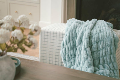 Hugs Willow Blue textured blanket draped over a chair with a neutral background.