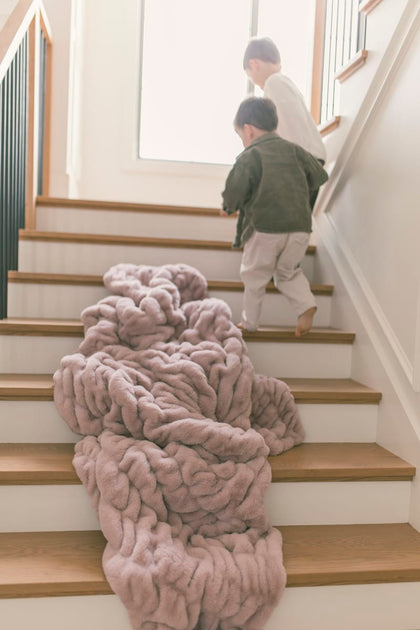 Two children walking up stairs near a soft, plush Hugs Heirloom Rose Blanket draped on the steps.