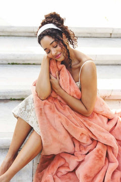 A woman cozying up with the Lush Tawny Spice Blanket in a beautiful coral hue, showcasing its plush texture.