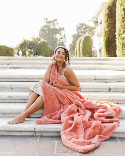 Woman sitting on stairs wrapped in Lush Tawny Spice Blanket, showcasing its plush texture and coral hue.