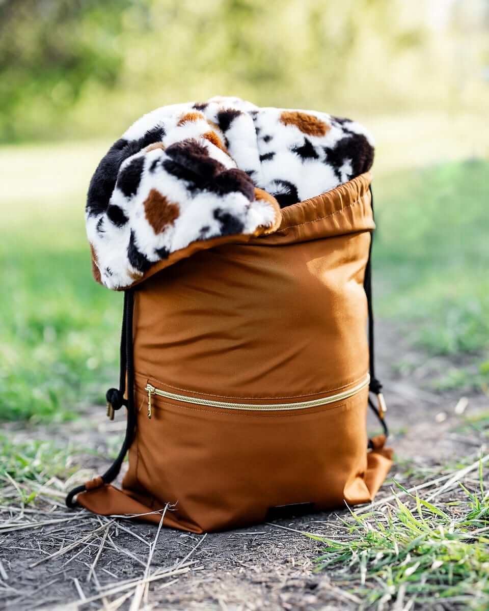 Everywhere Blanket Brown Cow rolled into a stylish brown backpack, perfect for outdoor adventures and picnics.