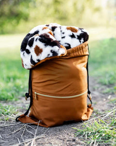 Everywhere Blanket Brown Cow rolled into a stylish brown backpack, perfect for outdoor adventures and picnics.