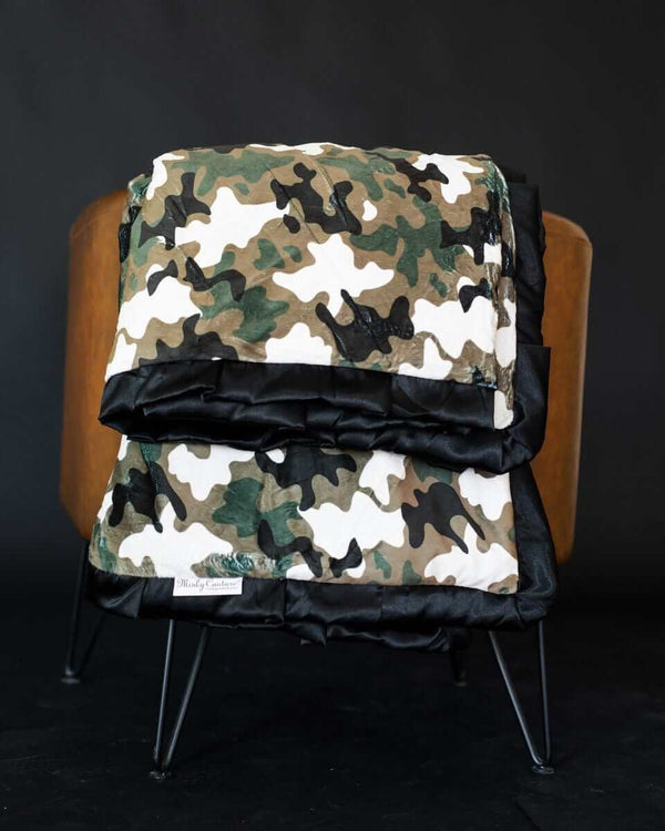 Camo Blanket folded on a chair showcasing its stylish design and plush black backing.