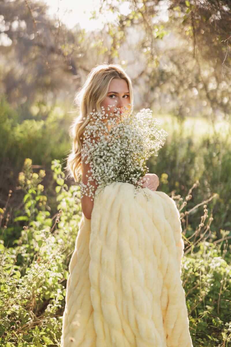 Minky Couture Hugs Butter Yellow Blanket wrapped around woman holding flowers in a sunny outdoor setting.