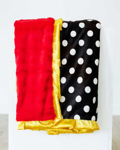 Happiest Blanket with white polka dots on a black background and plush red backing, featuring a golden yellow satin ruffle.