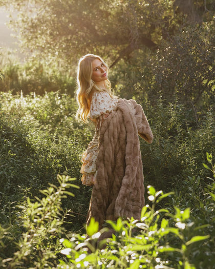 A woman in a sunny outdoor setting holds a Hugs Milk Chocolate Blanket, showcasing its plush texture and warm brown color.