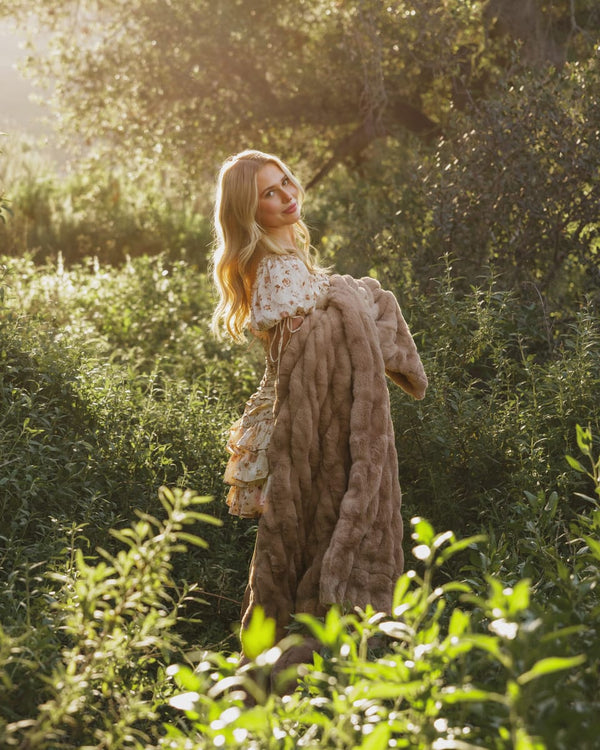 A woman in a sunny outdoor setting holds a Hugs Milk Chocolate Blanket, showcasing its plush texture and warm brown color.
