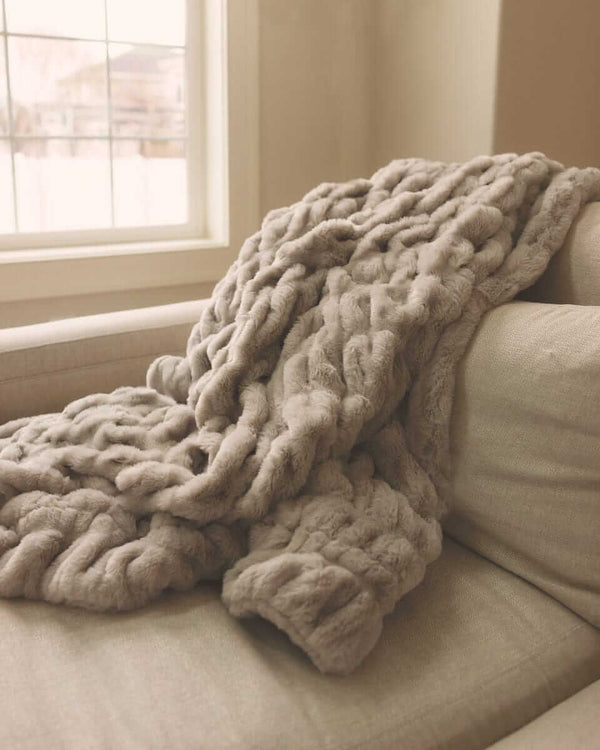 Close-up of a faux fur Minky Couture blanket draped over a light-colored sofa in a bright, cozy living room.