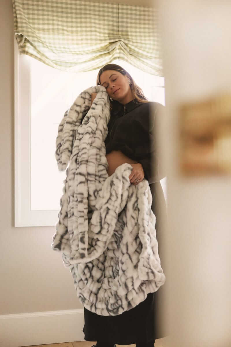 Woman holding a plush Minky Couture blanket near a window, highlighting its soft texture and cozy drape in natural light.
