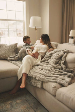 Mother and child relaxing on a sofa wrapped in a plush Minky Couture blanket in a warm, cozy living room.