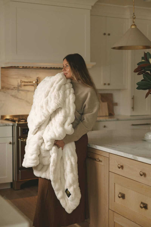 Woman standing in a kitchen holding a plush Hugs Angel Minky Couture blanket with a soft, cozy drape