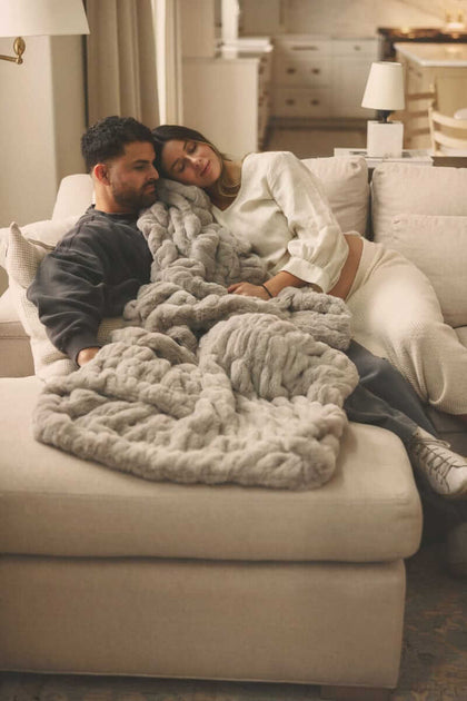 Couple cuddling on a sofa under a soft Hugs Haven Gray Minky Couture blanket in a calm, cozy living room.