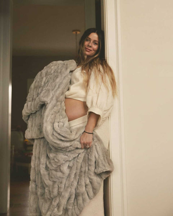 Woman standing in a doorway holding a plush gray Minky Couture blanket, styled in a soft, cozy home setting.