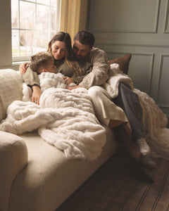 Family cuddling on a sofa under an ivory plush Hugs Angel Minky Couture blanket.