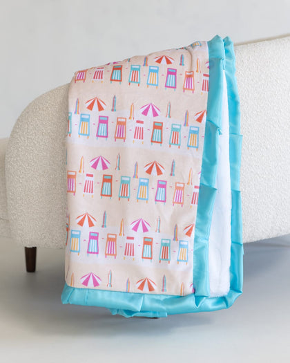 Colorful beach-themed blanket with a blue border draped over a chair.