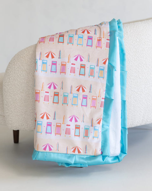 Colorful beach-themed blanket with a blue border draped over a chair.
