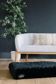 Black Crinkle Pet Crate Pad cover on a stylish floor near a modern couch with greenery in the background.