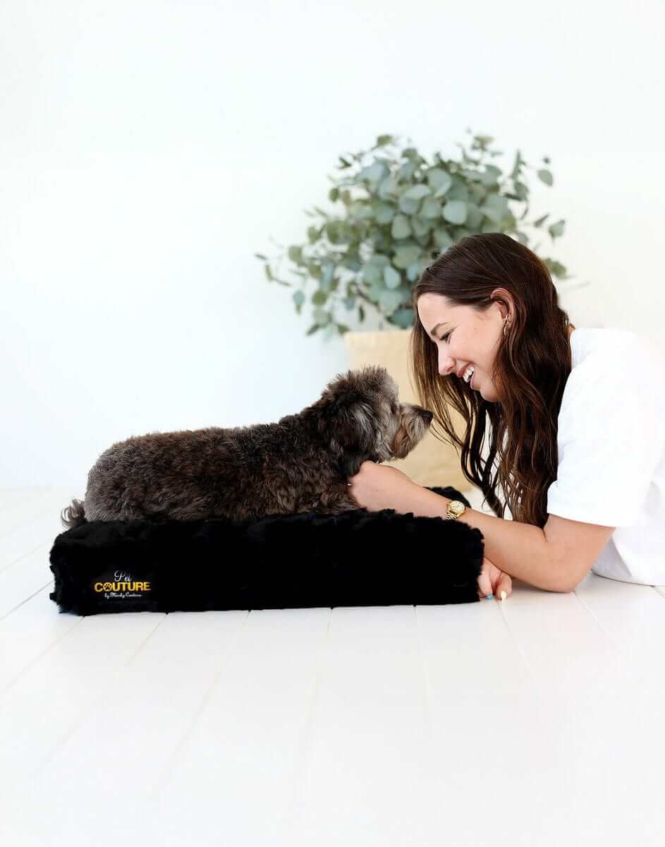 A woman enjoying time with her pet dog on a Black Crinkle Pet Crate Pad cover, showcasing comfort and style.