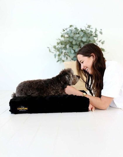 A woman enjoying time with her pet dog on a Black Crinkle Pet Crate Pad cover, showcasing comfort and style.