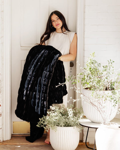 Model showcasing the Hugs Black Blanket, a plush and cozy fabric draped beautifully in a stylish room.