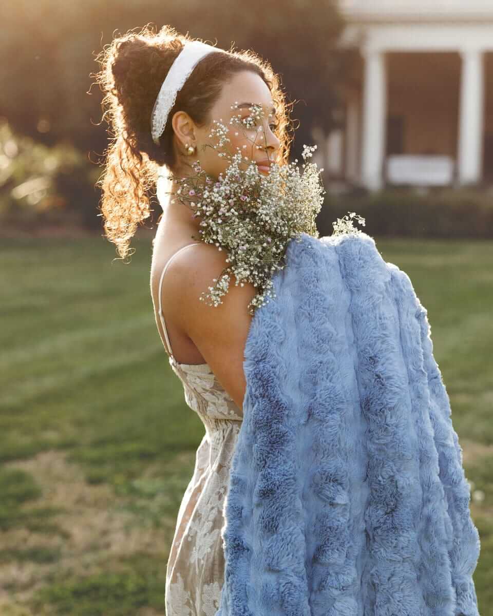 Model holding Ultra Sorbet Faded Denim Blanket while surrounded by nature, showcasing its cozy charm and texture.