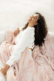 Woman enjoying the warmth of the Sorbet Blush Pink Blanket while relaxing on a cozy sofa.